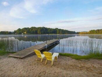 two yellow chairs on sand next to pier jutting out into calm lake
